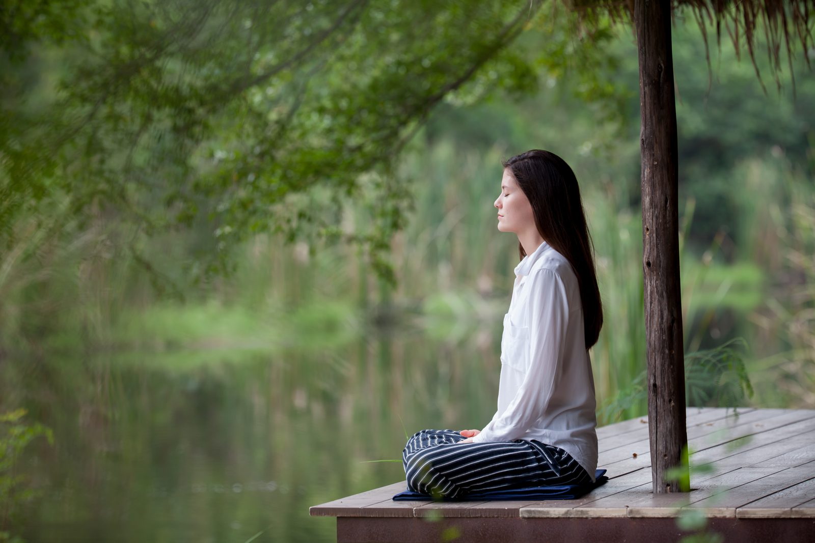 Žena v tichej meditácii na drevenom móle pri jazere